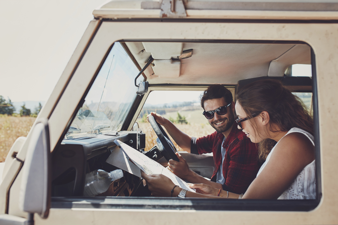 Man and woman on a road trip and reading a map together while seated inside their car. Happy young couple going on road trip.